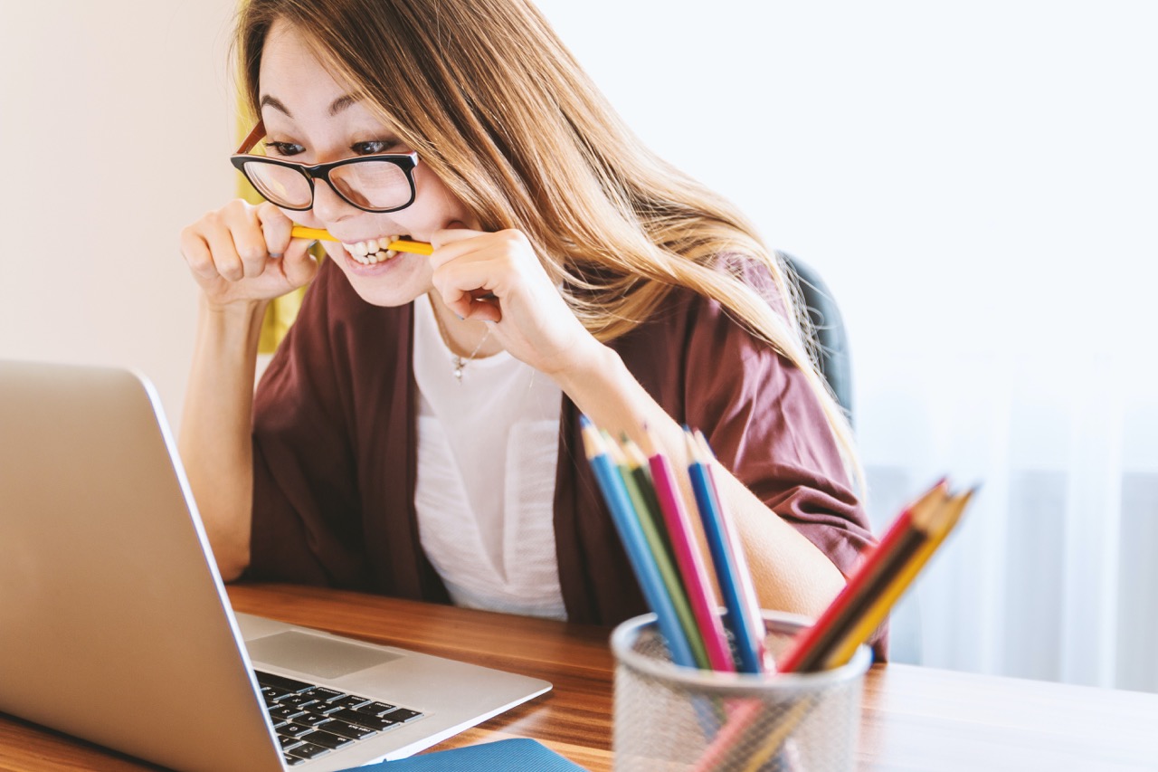 Anxious woman looking at laptop screen while biting on pencil.